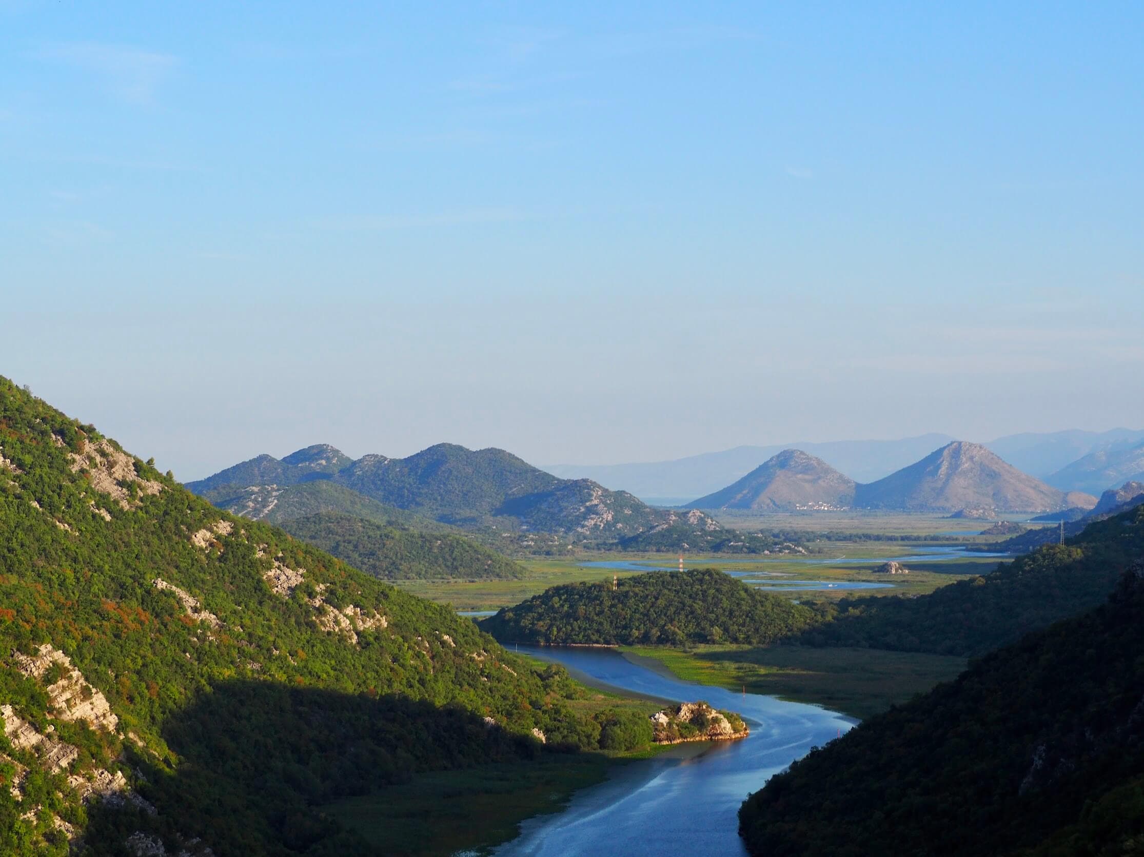 Colina boscosa reflejada en las aguas tranquilas del lago Skadar, Montenegro
